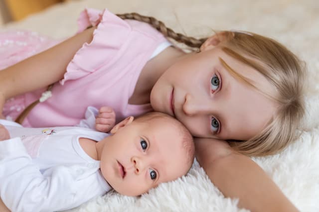 Newborn focení Brno se sourozencem, mladší sestra drží novorozené miminko v jemném světle, ateliér v Čechyni nedaleko Brna